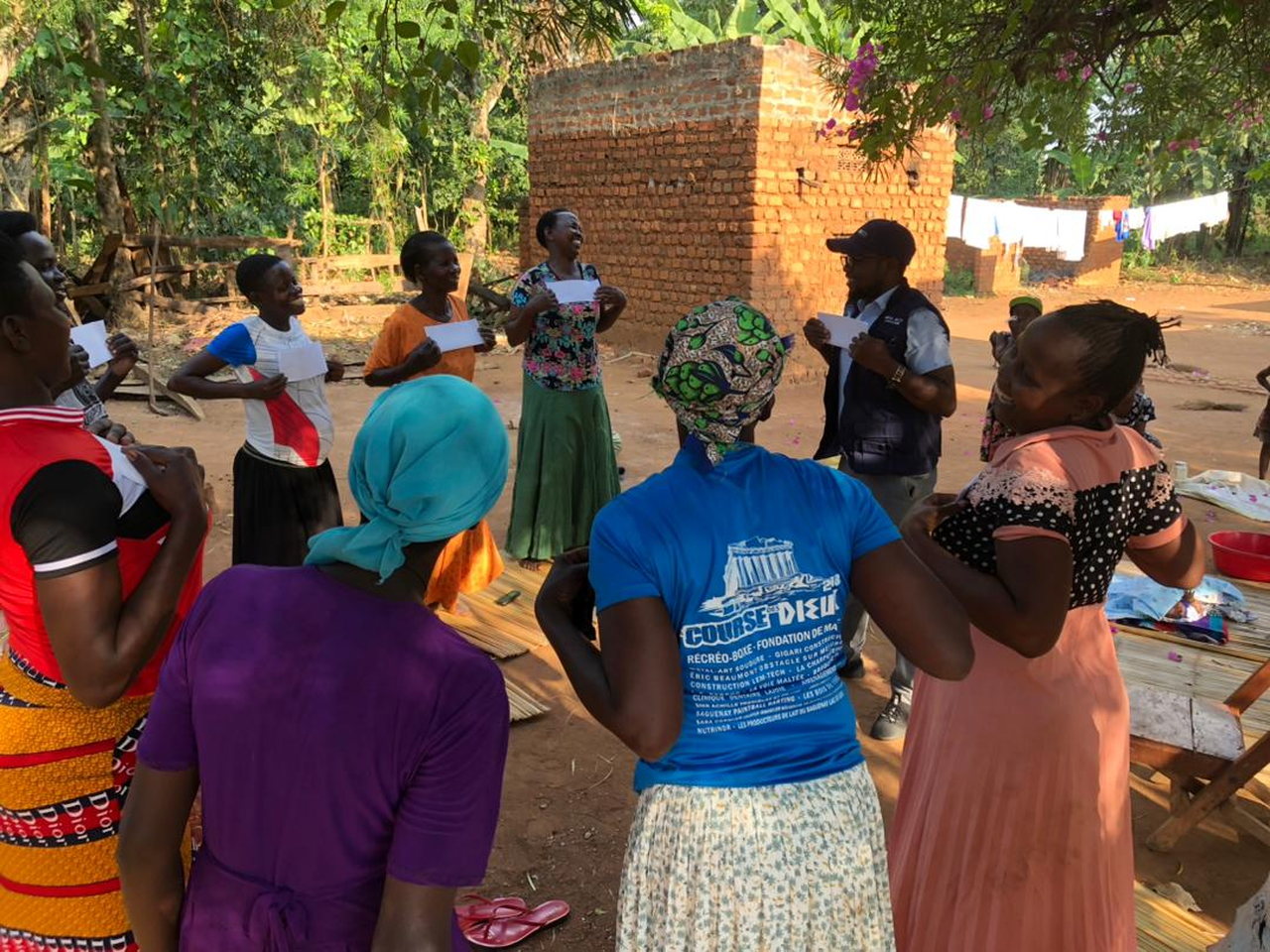 Community members take part in a group discussion outdoors beneath trees.