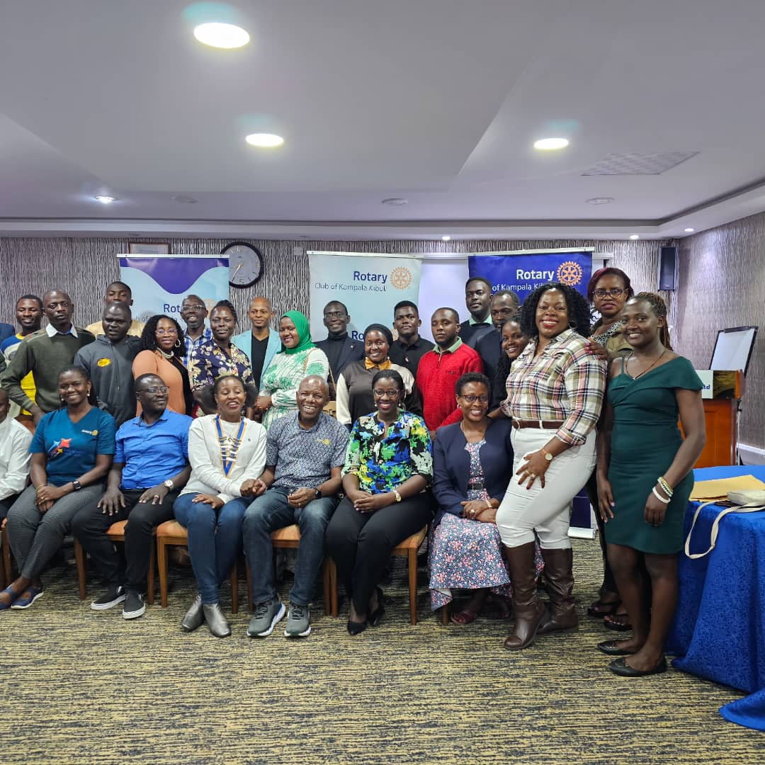 Participants pose for a group photograph beneath Rotary banners at an indoor meeting.